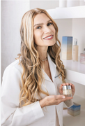 Woman in a white coat holding a skincare product in a clinical setting